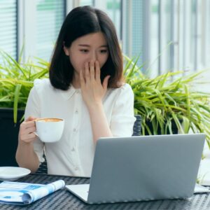 A person covering their mouth in surprise while looking at a laptop