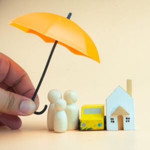 Little block people with a house and car under an umbrella